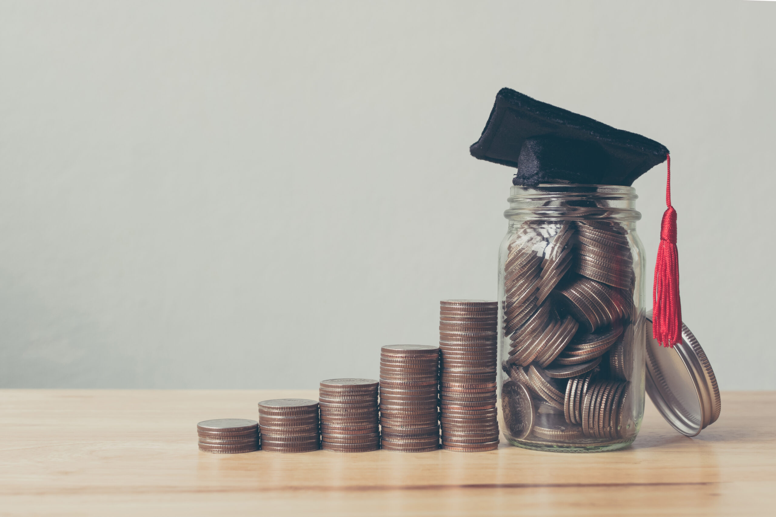 Coins in jar with money stacked and grad cap